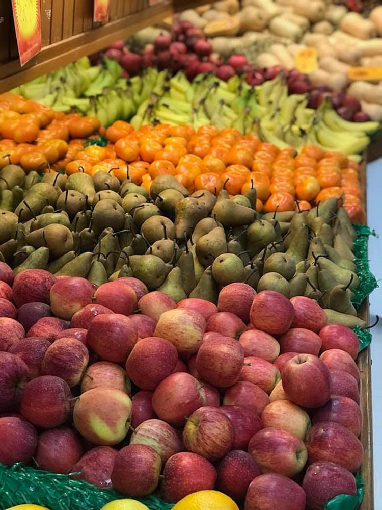 Fruit display in a market with apples, pears, and oranges arranged in neat rows on green trays.